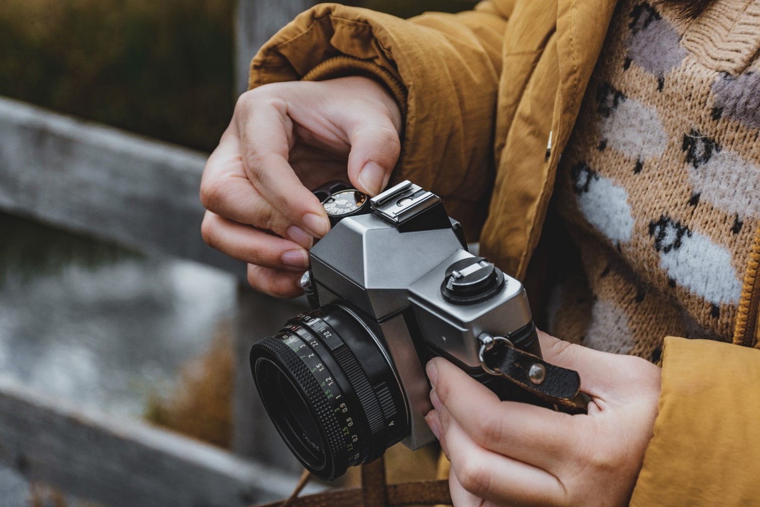 woman's hand holding camera, she is wearing a yellow coat and sweater