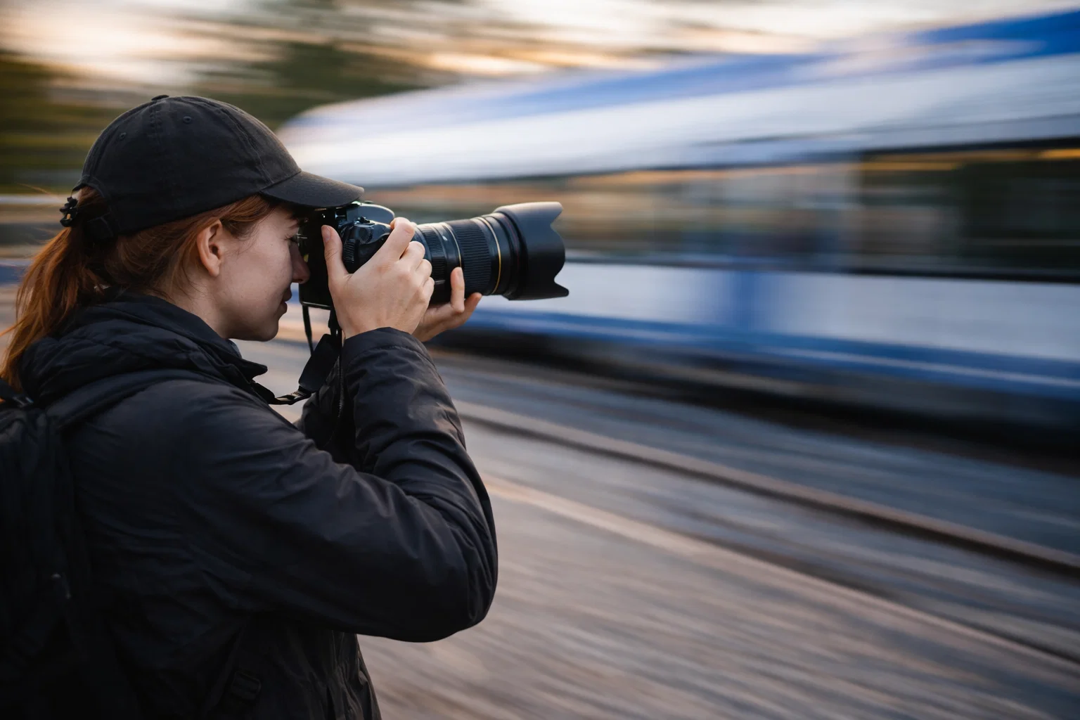 A woman demonstrating panning in photography by following a train with her camera whilst standing on a platform