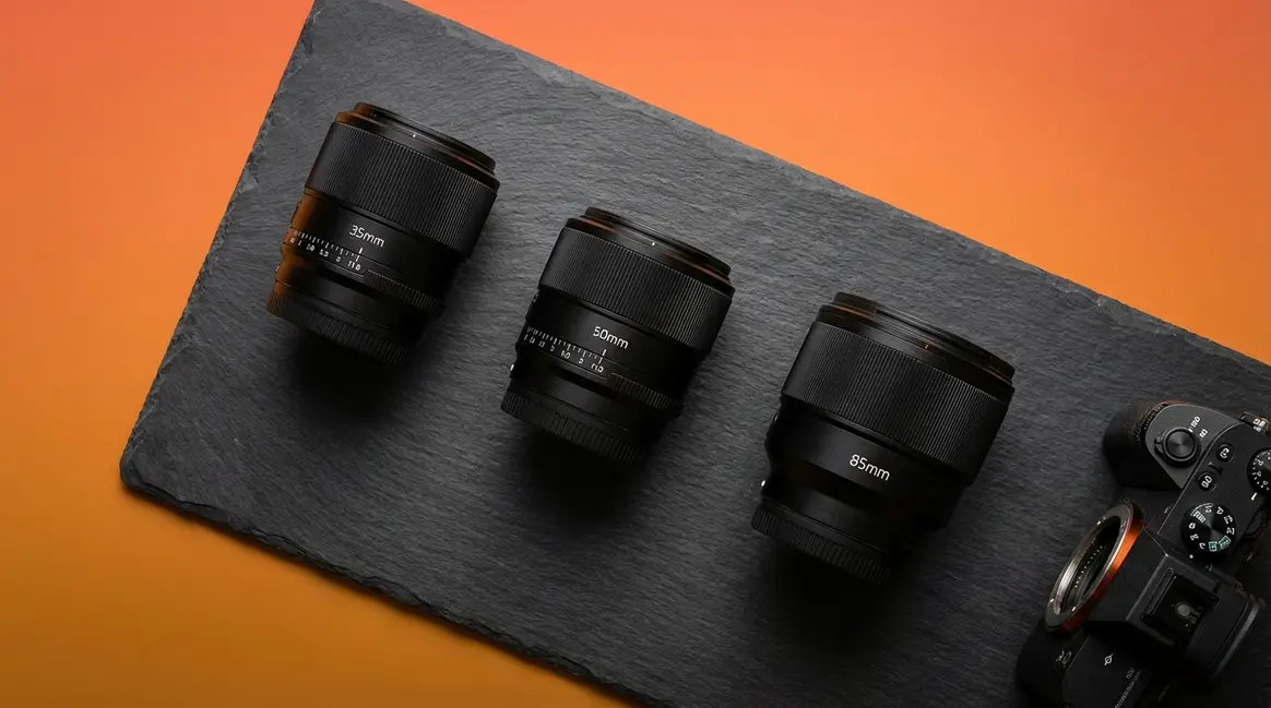 Photography prime lenses 35mm 50mm and 85mm arranged beside a mirrorless camera body