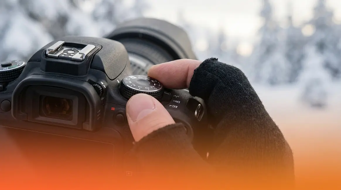 Photographer adjusting exposure compensation dial to fix underexposed snow photography