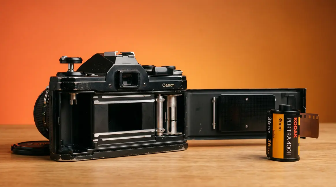 How to change film in a camera showing open 35mm SLR with film canister beside it